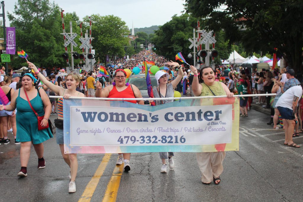 Students from the UCO womens, gender and sexuality studies program walk the Northwest Arkansas Pride Parade in holding banner for the Elder Tree Women's Center