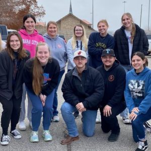 14 Students in a row smiling. The barbed wire fence of Federal Corrections Institution El Reno can be seen in the background.
