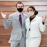 Two UCO student wearing masks and professional suits display the traditional "hooves up" school spirit hand gesture.